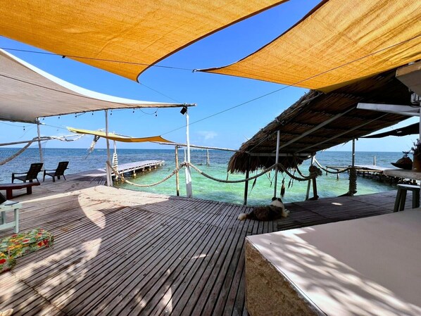 A wooden deck with a thatched-roof structure, a wooden pier extending into the water, and clear blue skies.
