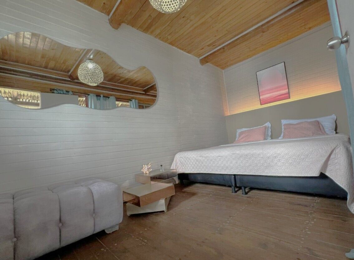 Un dormitorio con cama, mesitas de noche, sofá, techo de madera y un espejo montado en la pared.