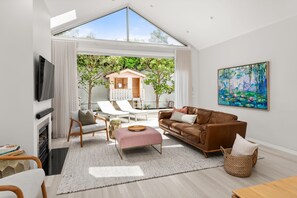A modern living room with a large window, a brown leather sofa, a wooden coffee table, and a painting on the wall.