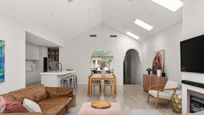 Ein modernes Wohnzimmer mit einer Ledersofa, einem pinkfarbenen Hocker und einem Essbereich mit Holztisch und Stühlen.