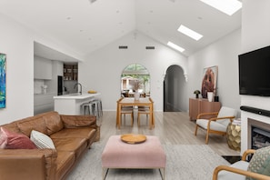A modern living room with a leather sofa, a pink ottoman, and a dining area with a wooden table and chairs.