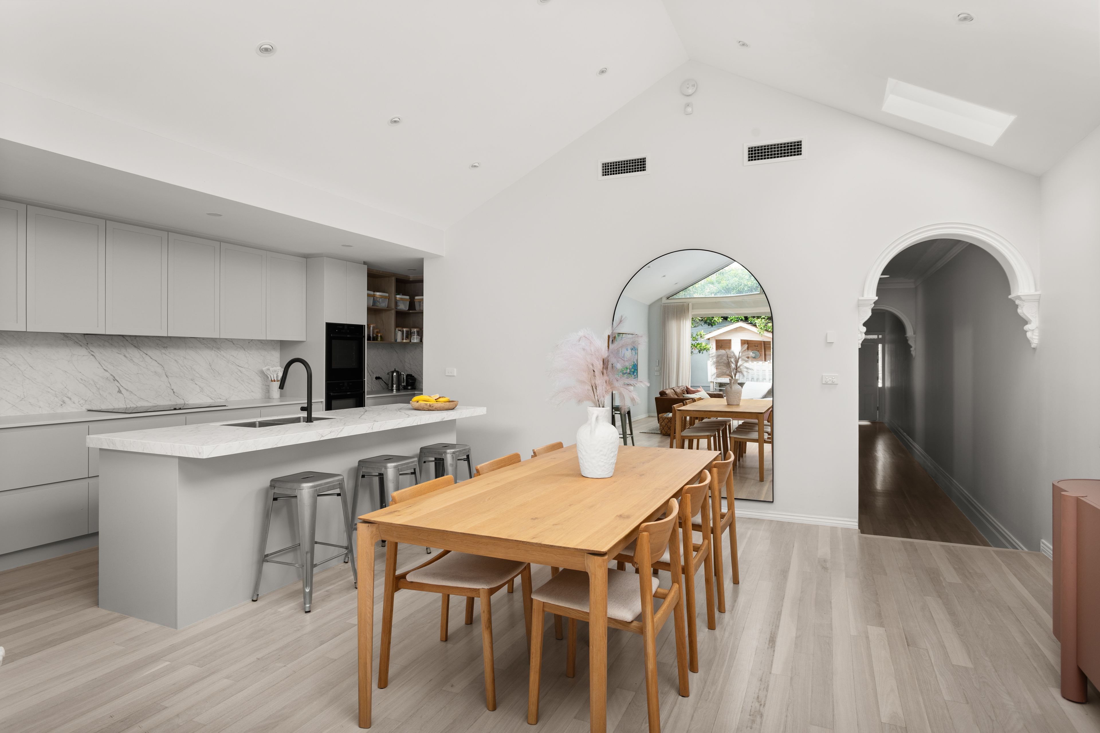 A modern kitchen with a marble countertop, a wooden dining table, and bar stools.