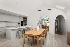 A modern kitchen with a marble countertop, a wooden dining table, and bar stools.