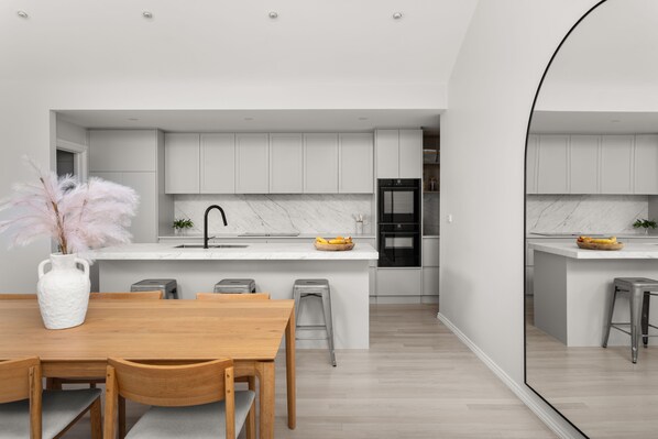 A modern kitchen with white cabinetry, a marble countertop, and a central island with stools.