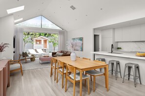A modern kitchen with white cabinets, a marble countertop, and a dining area with a wooden table and chairs.
