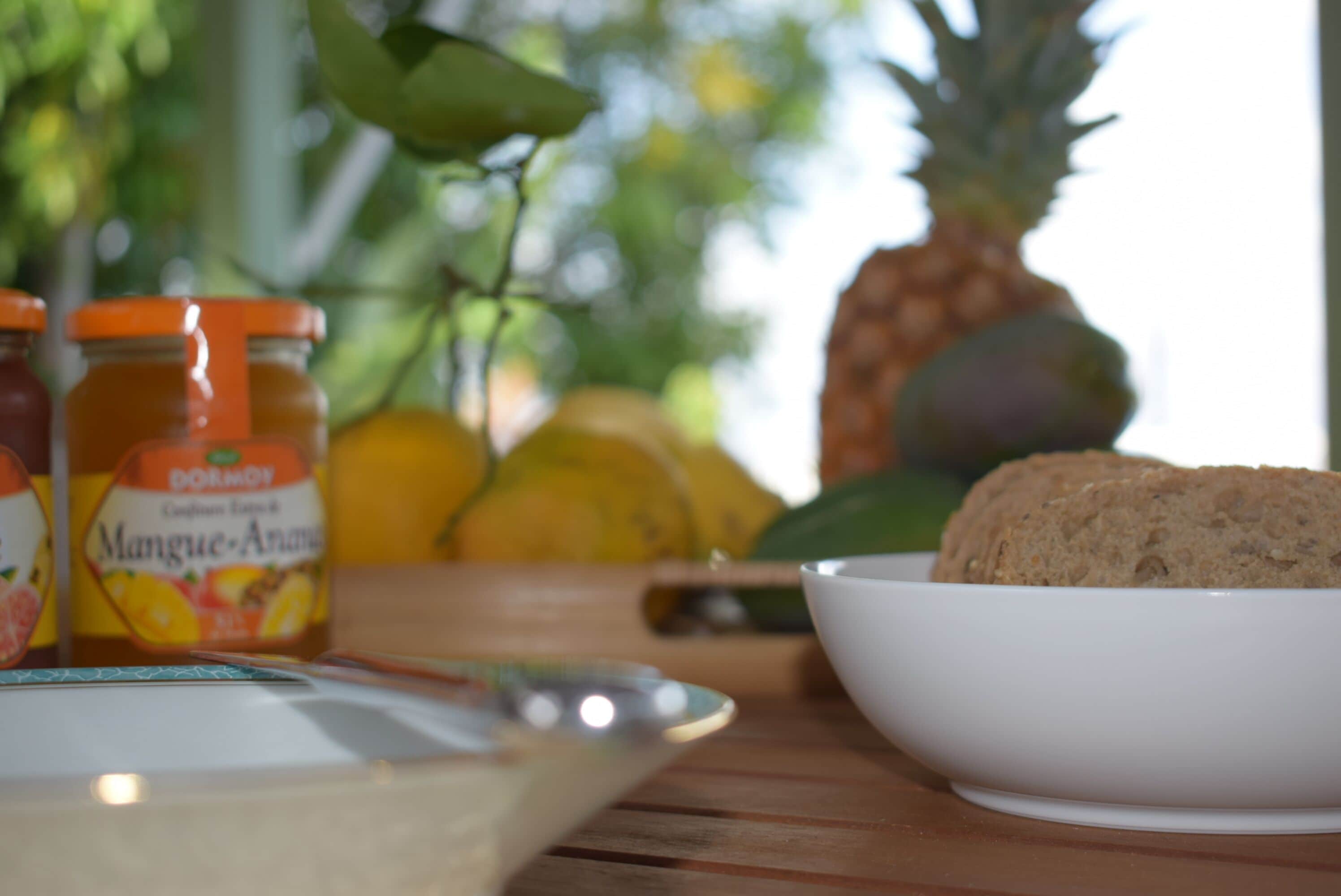 A wooden table with a white bowl, jars of honey, and a pineapple.