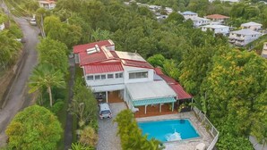 A house with a swimming pool, surrounded by lush greenery and a paved driveway. - Notre Vie Là (Le Robert)