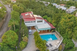 Una casa con piscina, rodeada de exuberante vegetación y un camino de entrada pavimentado.