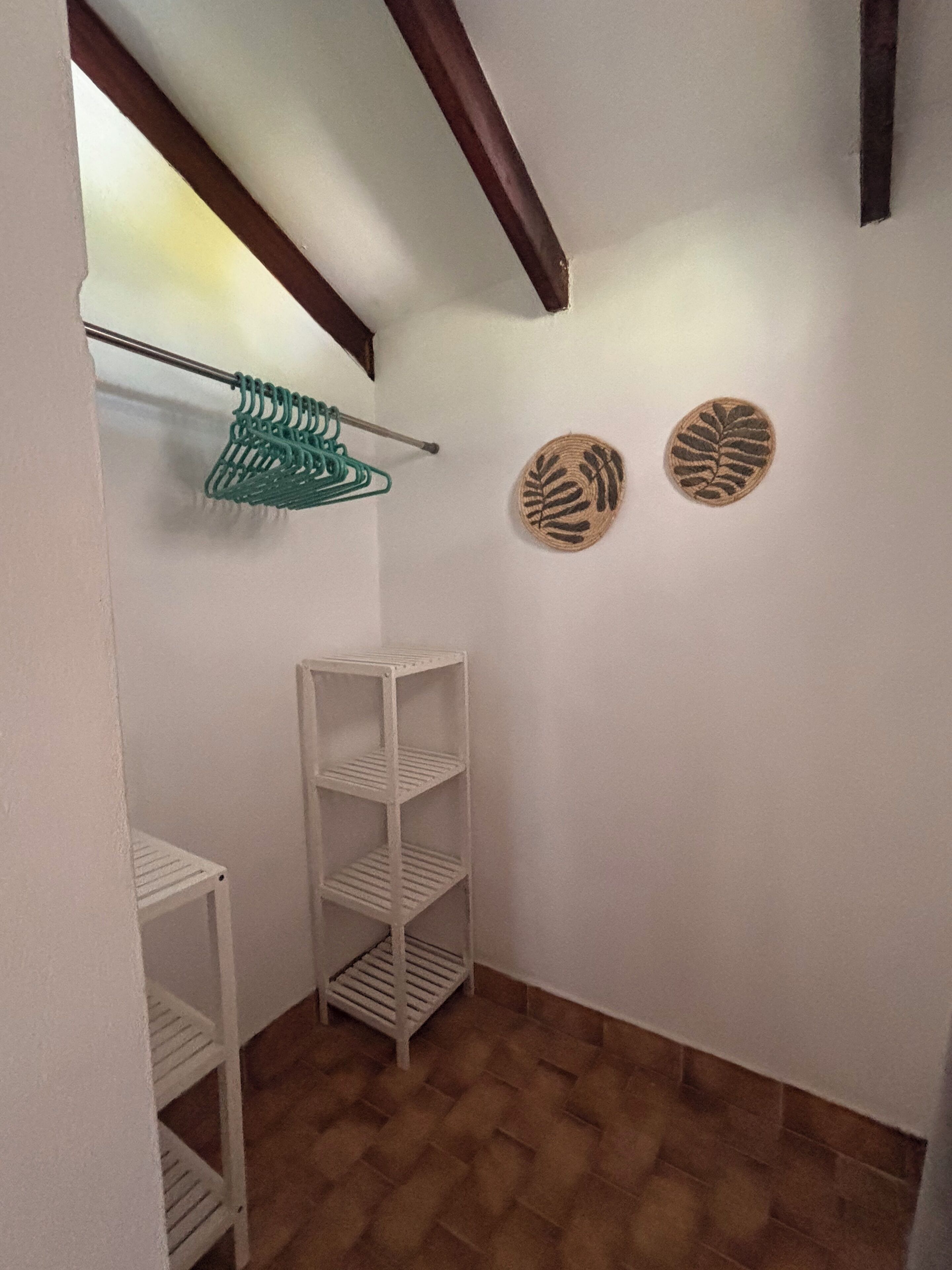 A corner room with a white wall, a wooden ceiling beam, a white shelving unit, and a patterned rug.