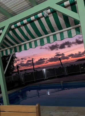 A covered outdoor area with a pool, a fence, and a sunset view. - Notre Vie Là (Le Robert)