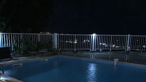 A nighttime swimming pool with a stone-tiled deck and a white metal fence. - Notre Vie Là (Le Robert)