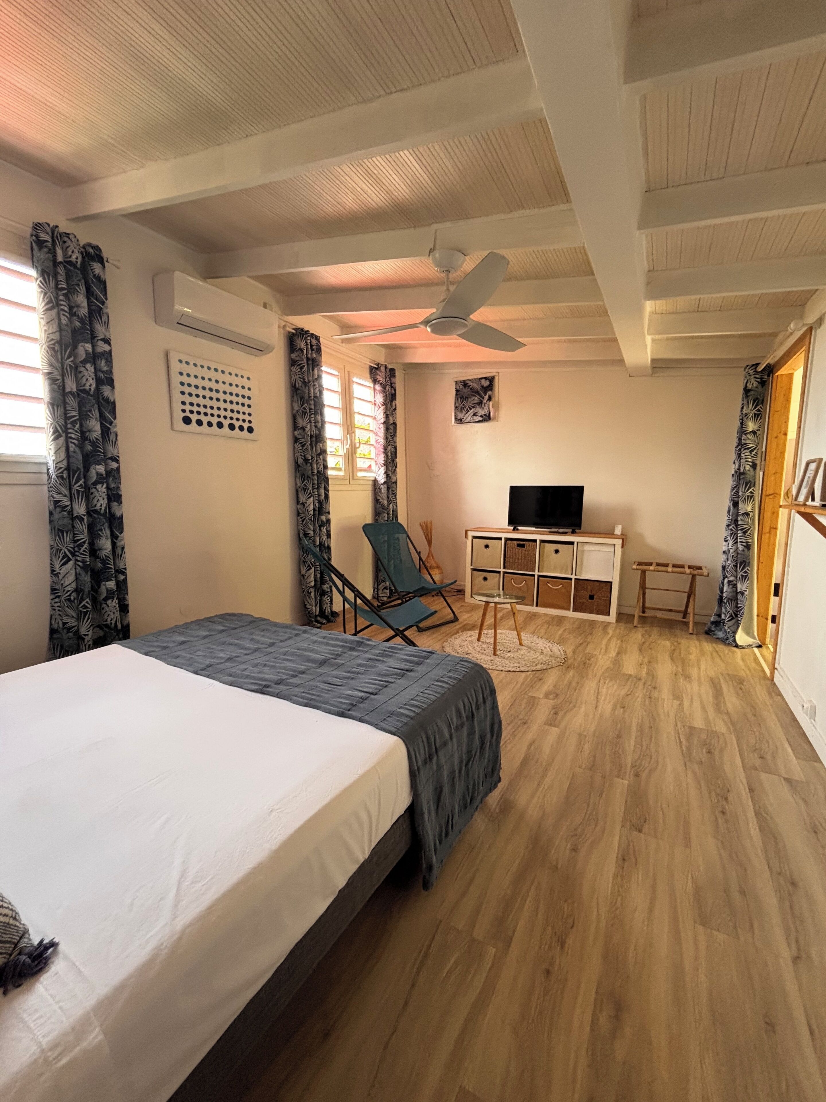 A bedroom with a bed, a desk, a chair, a TV, and a ceiling fan.