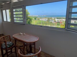 A balcony with a view of a beach and houses. There is a wicker table and two wicker chairs with cushions.