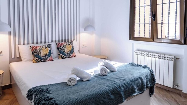 A neatly made bed with a blue blanket and rolled towels, a window with bars, and a radiator. - Spacious, modern, and central 2-bedroom apartment with 1 bathroom in Madrid (Madrid)