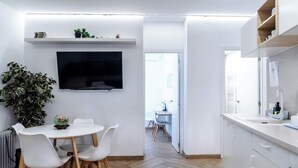 A modern kitchen with a dining area, white cabinetry, a flat-screen TV, and a potted plant. - Spacious, modern, and central 2-bedroom apartment with 1 bathroom in Madrid (Madrid)