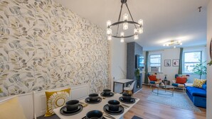 Un soggiorno moderno con zona pranzo, caratterizzato da carta da parati decorata, un lampadario e un divano blu.