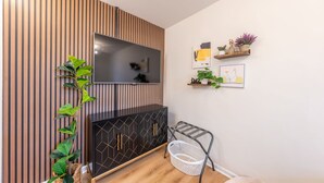 Un soggiorno moderno con una TV montata su una parete in legno, un mobile contenitore nero con motivi geometrici, una pianta e un cesto per la biancheria.