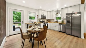 Une cuisine moderne avec des meubles blancs, des appareils en acier inoxydable et un coin repas avec une table dressée pour quatre personnes.