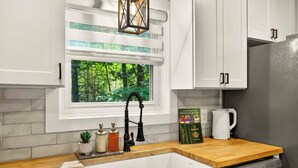 Une cuisine avec une fenêtre, des meubles blancs, un plan de travail en bois, un évier, une machine à café et un lave-vaisselle.