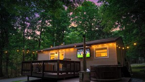 Une cabane avec une terrasse, un jacuzzi et un écran de télévision.