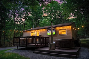 A cabin with a deck, a hot tub, and a TV screen.