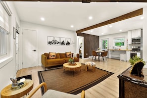 A modern living room with a sofa, coffee table, and dining area, leading to a kitchen with appliances.