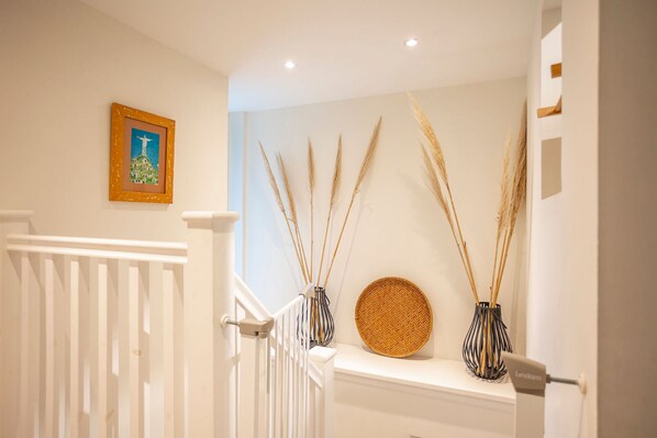 A staircase with a white railing, a framed picture on the wall, and two vases with tall reeds on a shelf.
