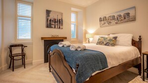 Une chambre à coucher avec un lit en bois, une cheminée et deux fenêtres équipées de stores.