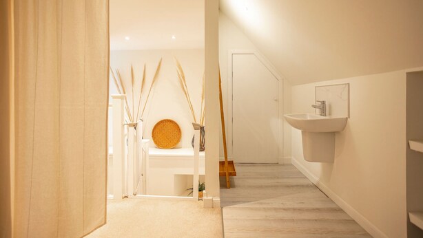 Une salle de bain moderne avec un plancher en bois, un lavabo blanc et un tapis rond en fibres naturelles posé sur une étagère.