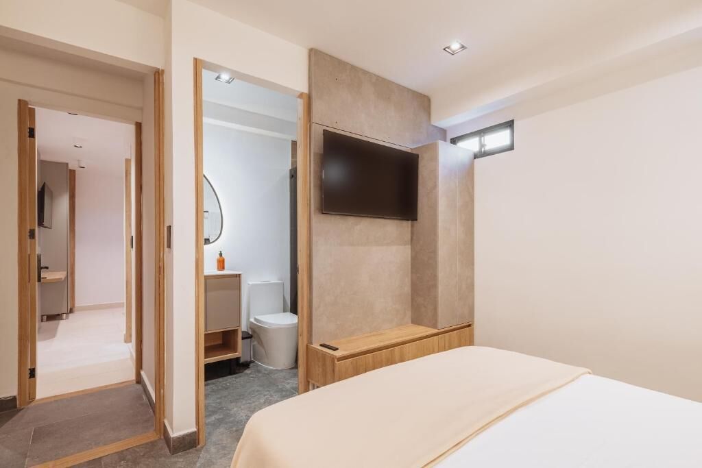 Una habitación de hotel moderna con una cama, un televisor montado en la pared, un banco de madera y un vestidor.