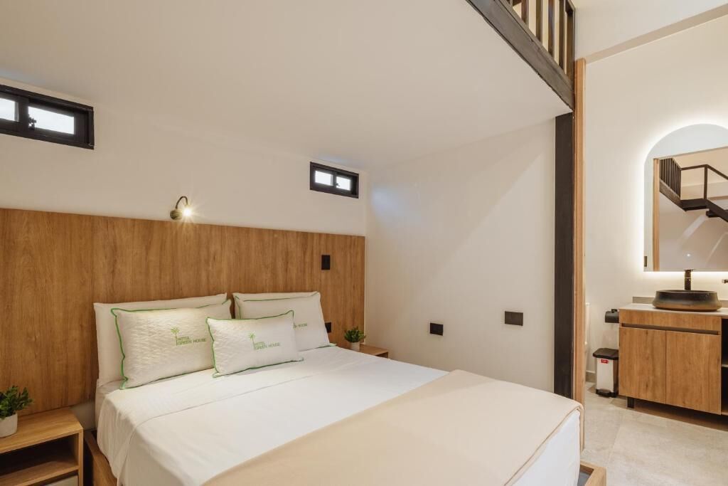 Une chambre d’hôtel moderne avec une tête de lit en bois, un lit avec une literie blanche, une petite table de chevet agrémentée d’une plante et un bureau intégré doté d’un miroir.