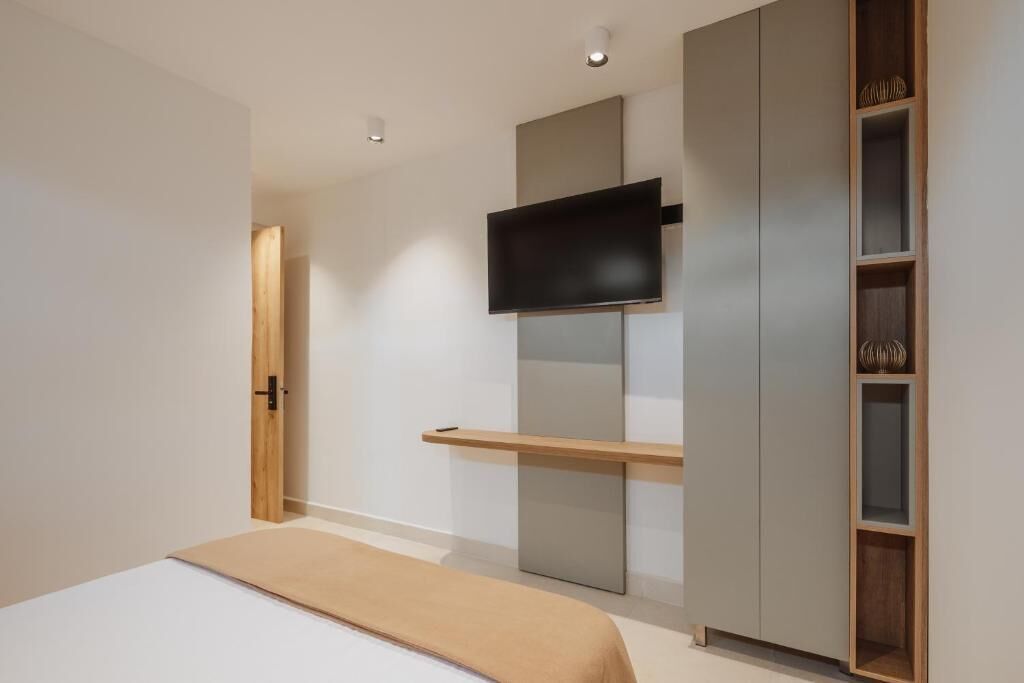 A bedroom with a bed, a TV mounted on a wall, a wardrobe, and a shelf with decorative items.