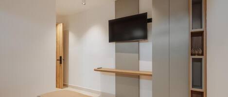 A bedroom with a bed, a TV mounted on a wall, a wardrobe, and a shelf with decorative items.