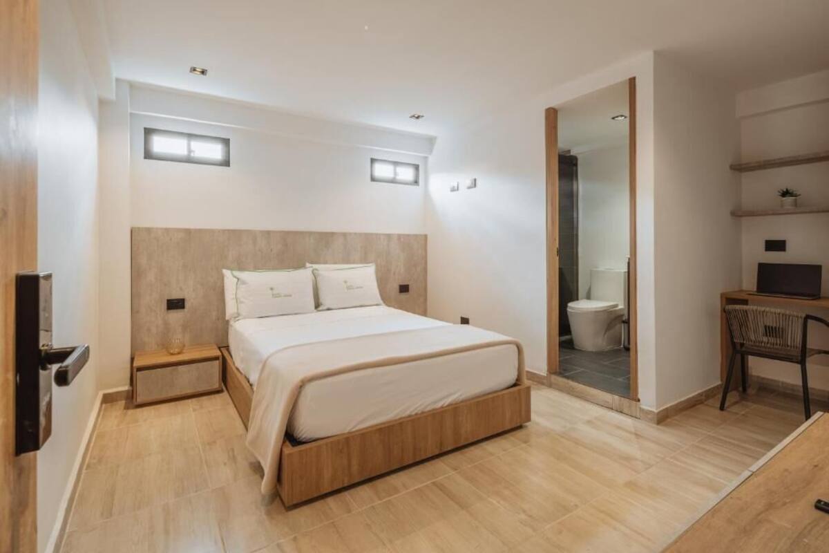 A modern bedroom with a wooden bed, bedside tables, a desk, and a bathroom visible through an open door.