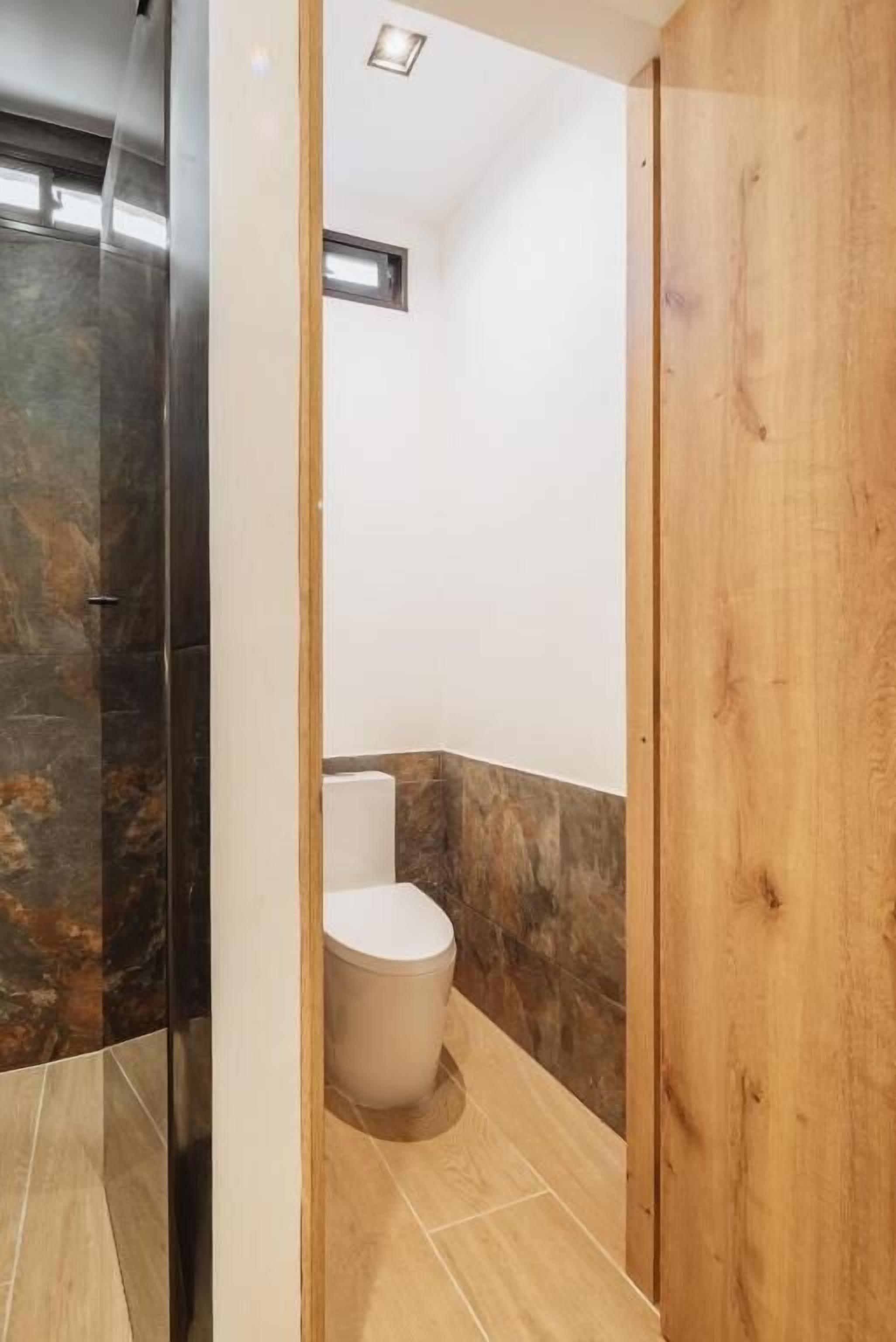 Un baño con inodoro, zona de ducha y puerta de madera.