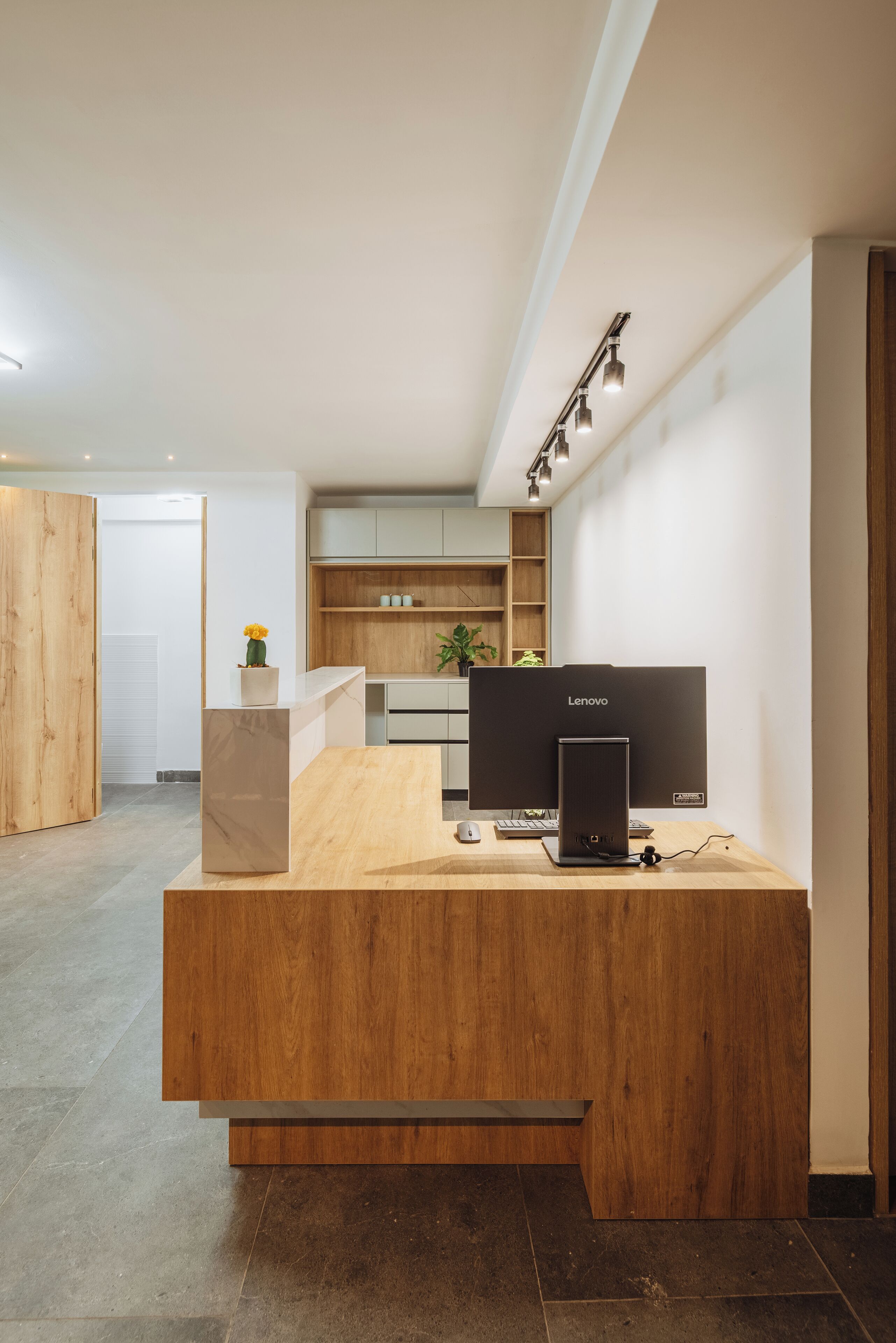 A modern reception desk with a wooden finish, a Lenovo computer, and a potted plant.