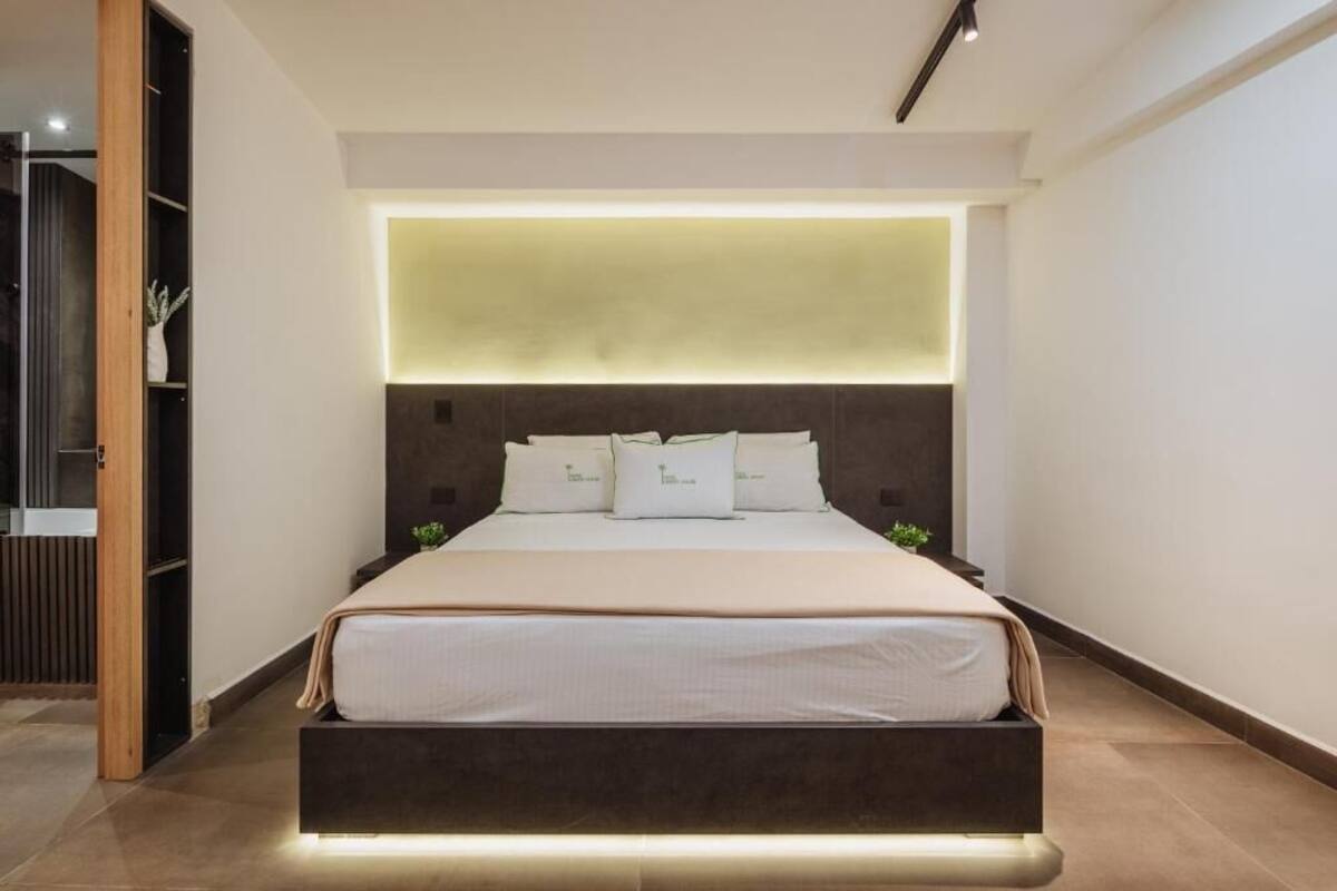 A modern bedroom with a bed, bedside tables, and a built-in light panel above the bed.