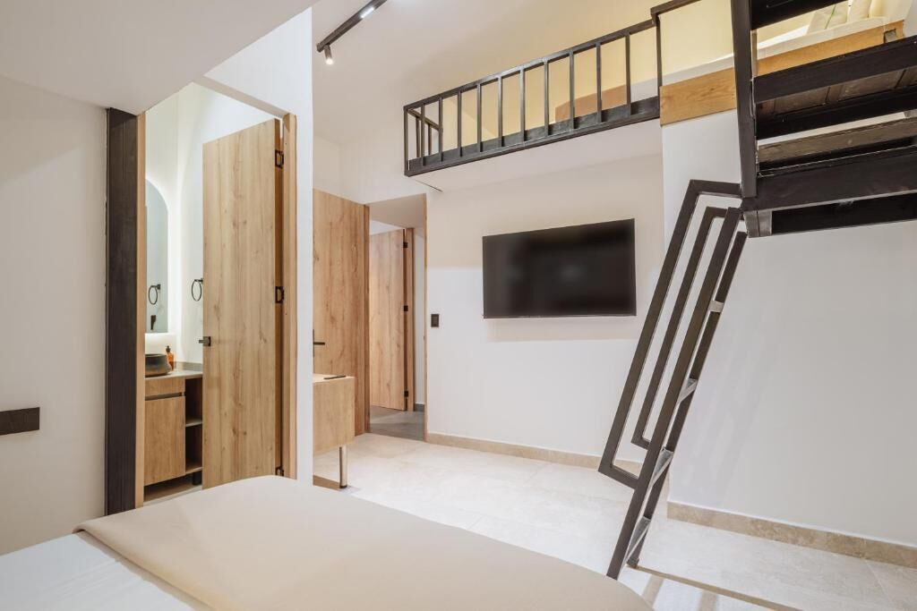 Une chambre à coucher avec un lit, un téléviseur fixé au mur, une armoire en bois et un escalier.