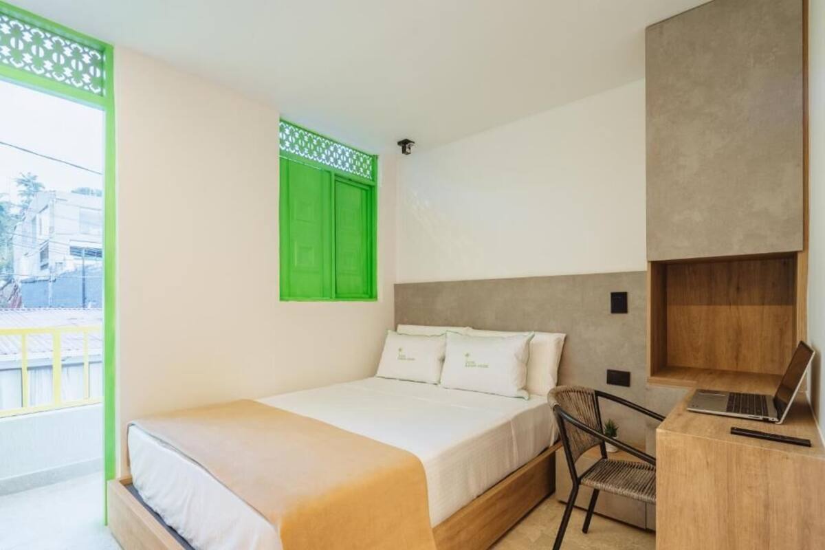 A bedroom with a bed, a desk with a laptop, a chair, and a window with green shutters.
