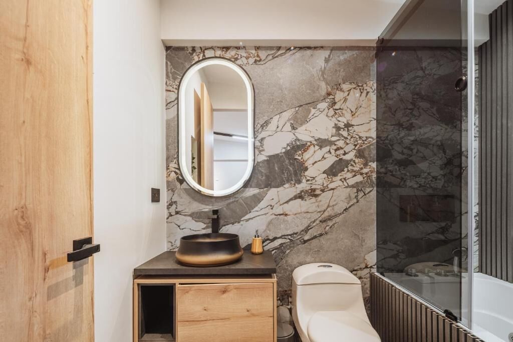 A bathroom with a marble wall, a round mirror, a sink, a toilet, and a bathtub.