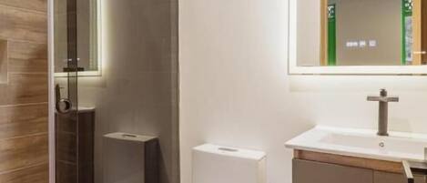 Un baño moderno con ducha de vidrio, inodoro blanco y tocador con espejo.