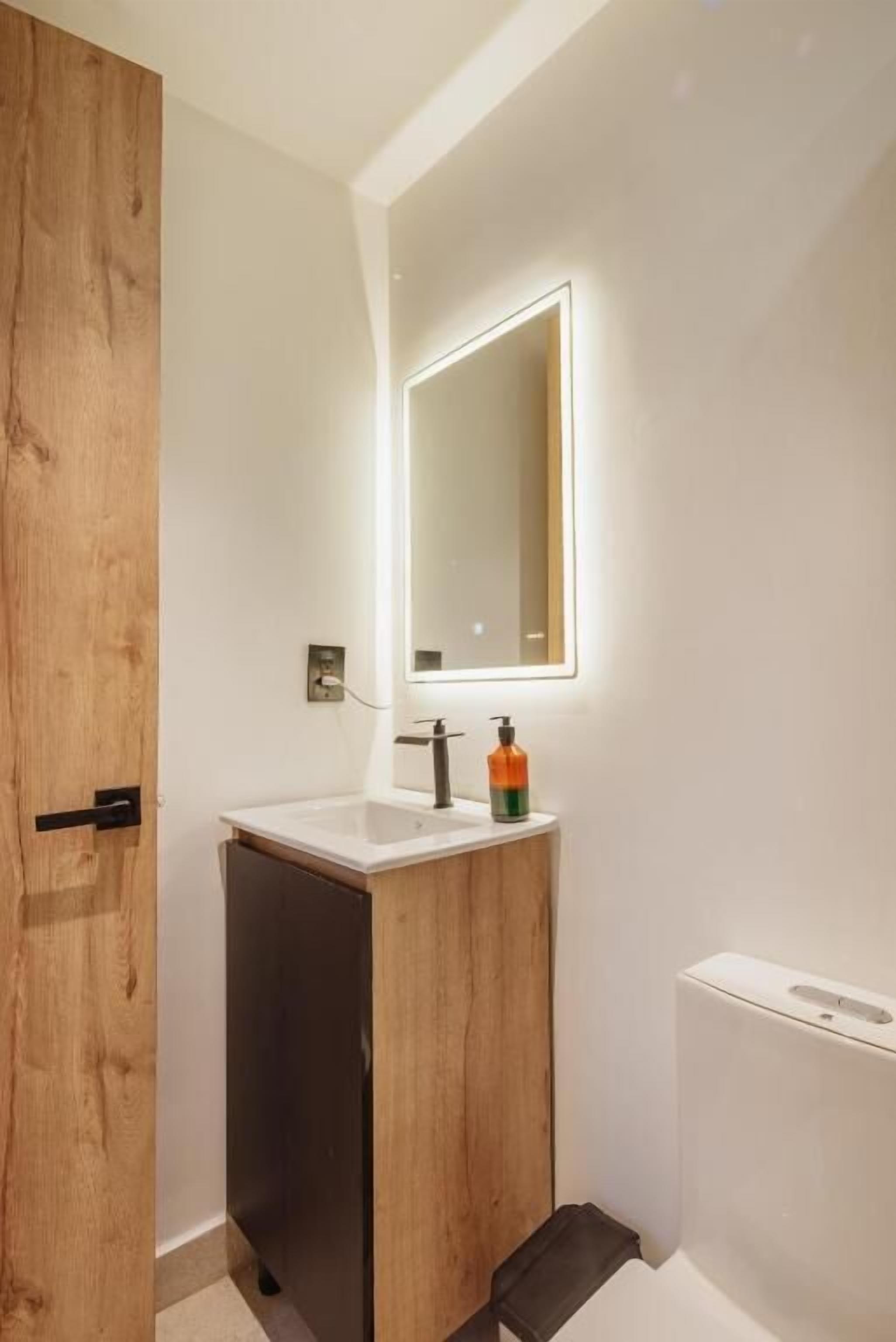 A bathroom with a wooden door, a white sink, a mirror, and a white toilet.