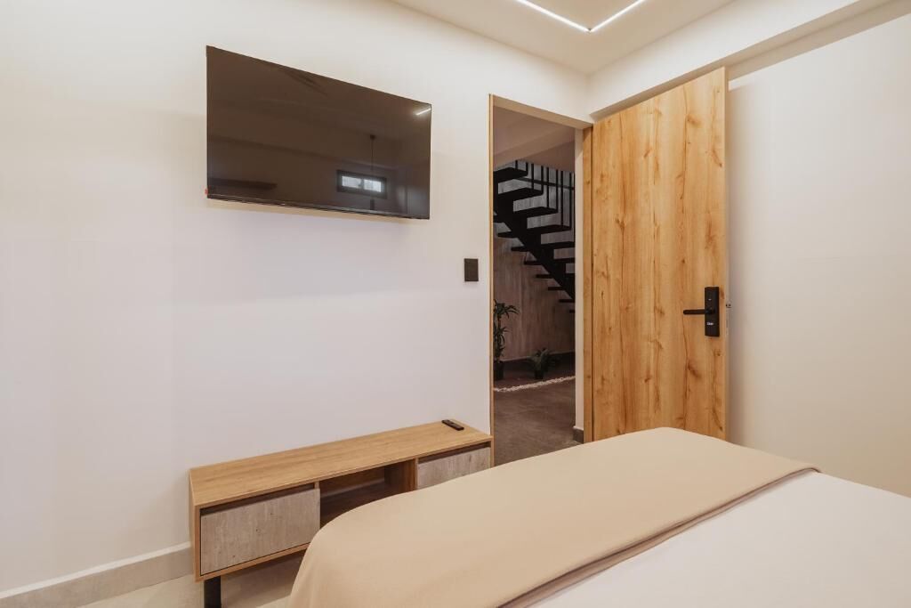 Un dormitorio con una cama, un banco de madera, un espejo y una puerta de madera que da a una escalera.