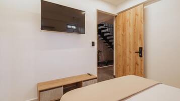 Un dormitorio con una cama, un banco de madera, un espejo y una puerta de madera que da a una escalera.