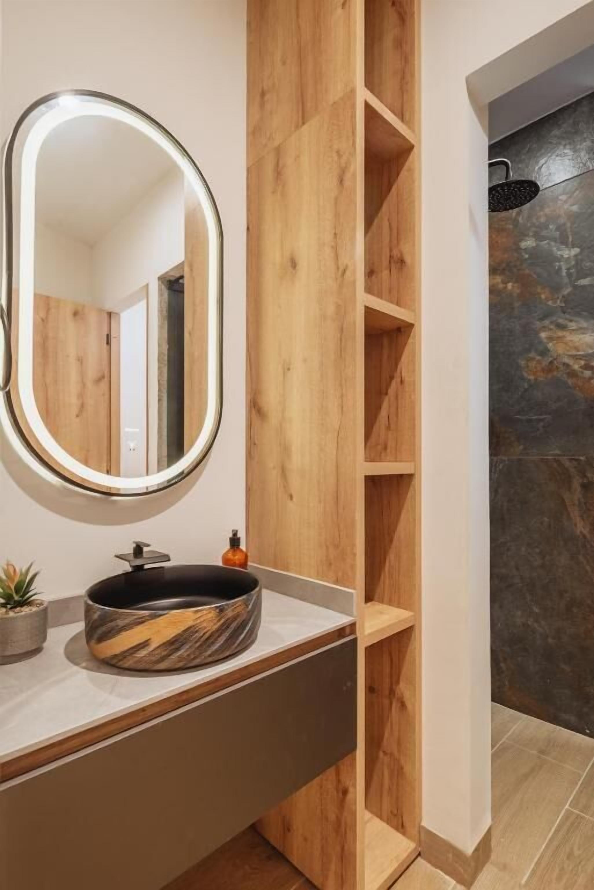 Een badkamer met een ronde spiegel, houten planken, een zwart wastafel en een stenen muur.