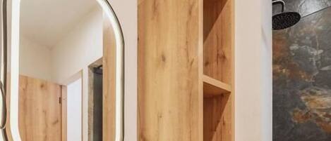 Een badkamer met een ronde spiegel, houten planken, een zwart wastafel en een stenen muur.
