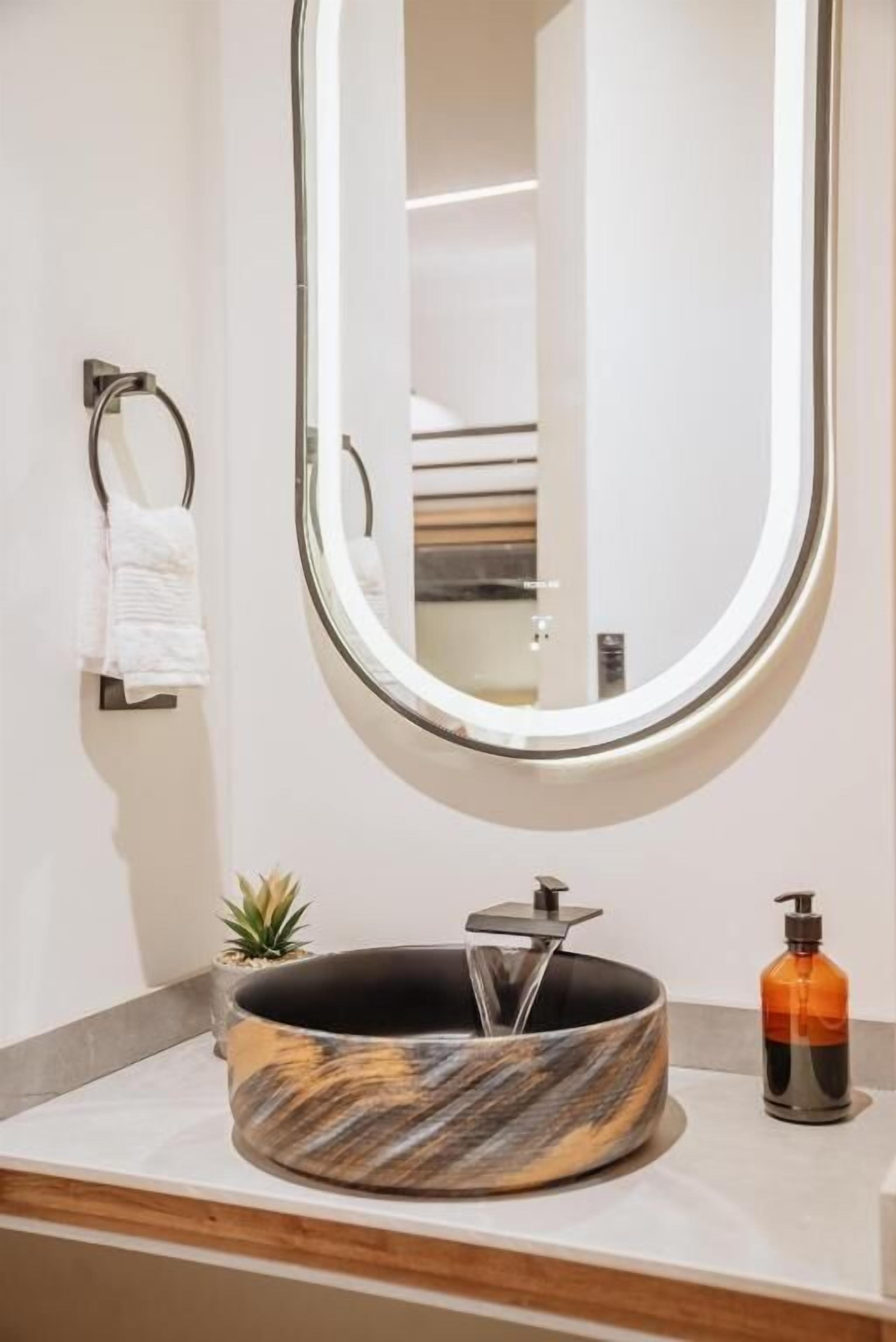 A modern bathroom with a round marble sink, a round mirror, a towel rack, and a small potted plant.