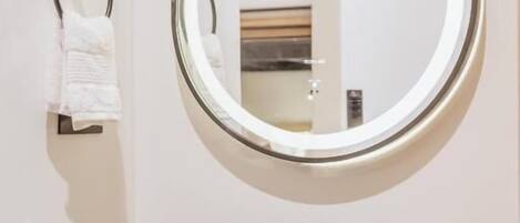 A modern bathroom with a round marble sink, a round mirror, a towel rack, and a small potted plant.