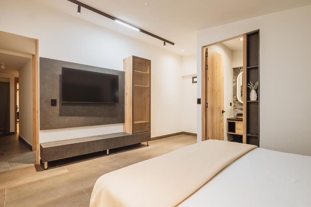 A modern bedroom with a large bed, a built-in TV, and a wooden wardrobe.