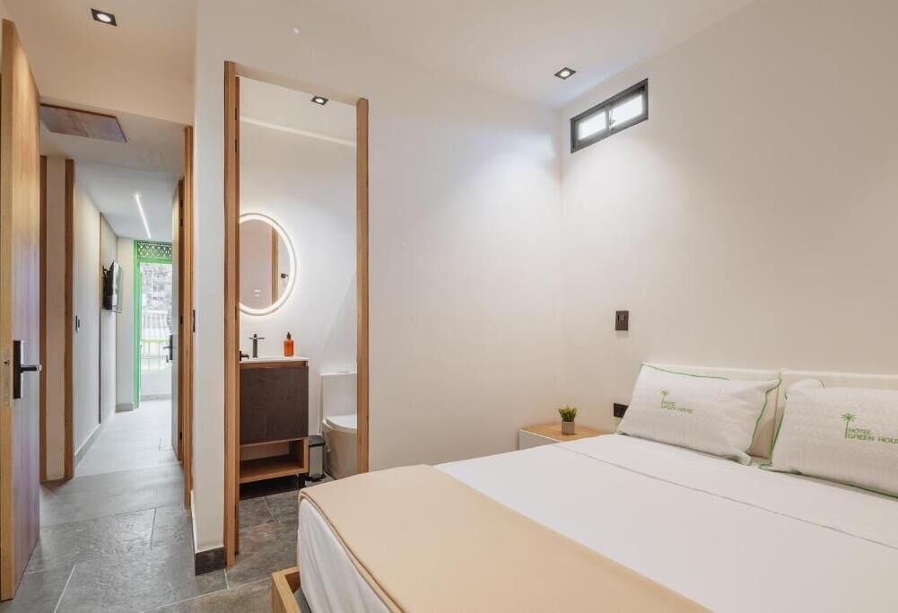 A hotel room with a bed, a bedside table, a mirror, and a view of the hallway.